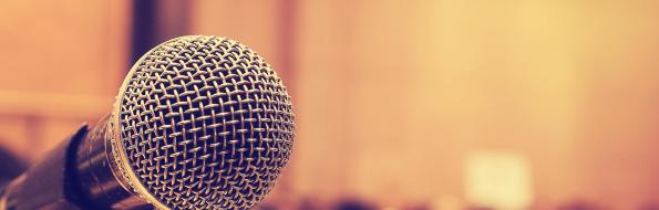 Microfono su palco con pubblico sfocato sullo sfondo.